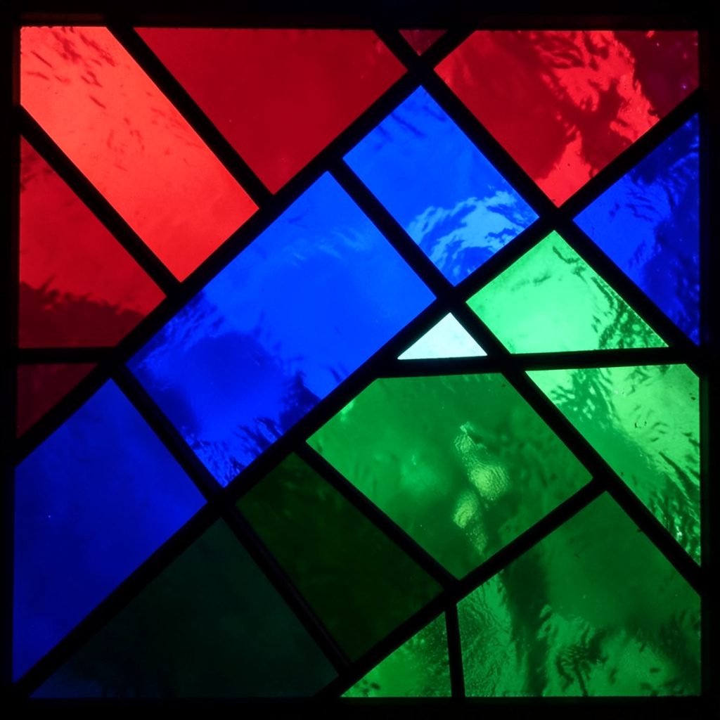 A stained-glass composition of national banners overlapping, ruby red, royal blue, and emerald green glass segments divided by thick black lead lines.
